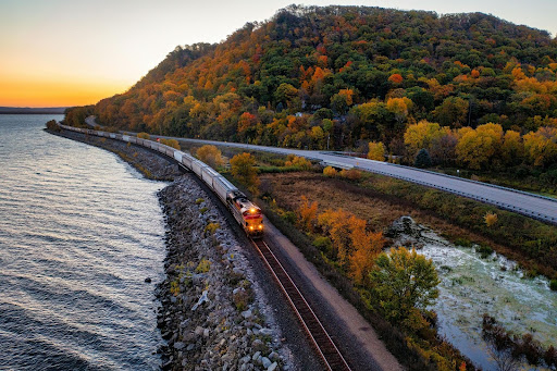 Train traveling along a coastal railway with autumn trees in the background.