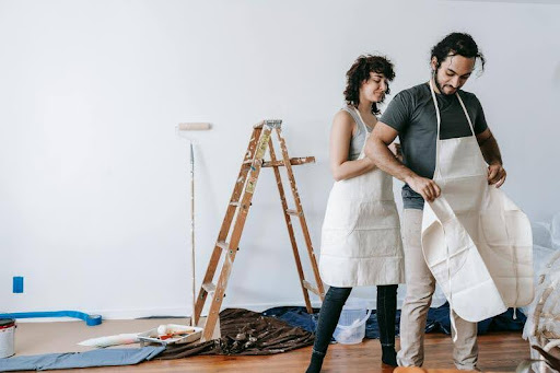 Couple wearing aprons painting a wall during a home renovation.