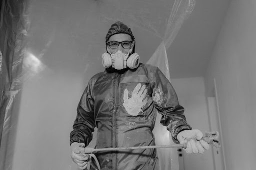 Person in a grey apron suit painting the exterior of a house.