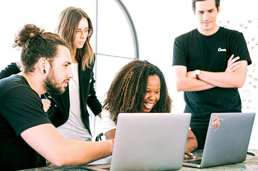 Group of coworkers gathered around a laptop in an office setting