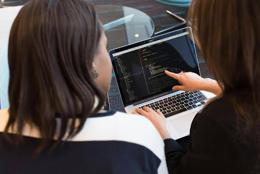 Woman pointing at laptop screen while discussing something with a colleague.