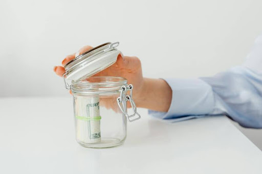 Person placing coins into a glass savings jar.