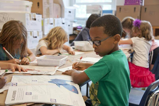 Children reading and writing at their desks in a classroom setting.