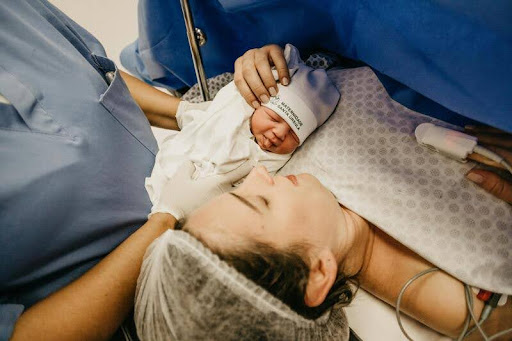 Woman in a maternity bed with newborn baby and nurse beside her