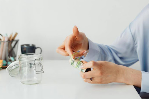 Person placing dollar bills into a glass savings jar