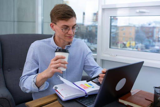 Businessman working on a laptop in an office while drinking coffee.