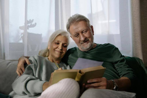 Elderly couple sitting together reading a book.