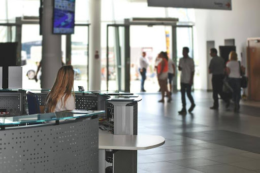 Woman working at a customer service desk with people entering and exiting the building.