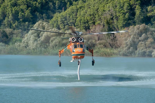 Firefighting helicopter flying over a river in Greece during wildfire response.