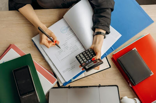 Person using a calculator with financial documents spread on a table.