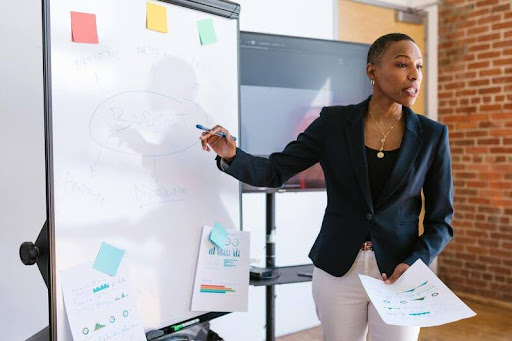 Woman pointing at a projector during a meeting, explaining a concept to colleagues.