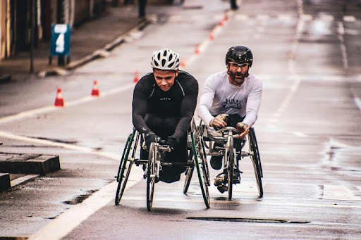 wo people with disabilities riding adaptive bicycles along a city street.
