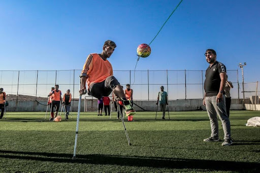 Man with a prosthetic leg playing soccer on a sunny field