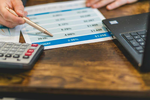 Person holding a pen next to an open laptop on a table