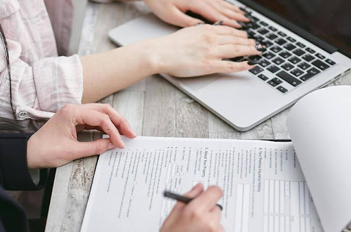Person signing a document while using a laptop