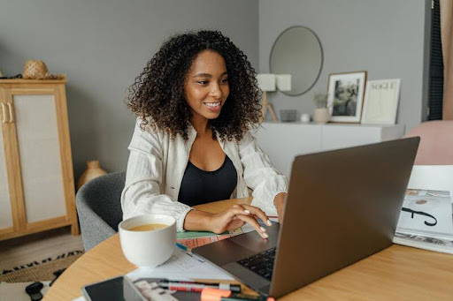 Woman working on a MacBook at a wooden table in a home setting.