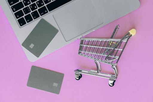 Shopping cart beside a laptop and smartphone on a desk.