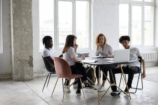 Four colleagues in an office gathered around a laptop, discussing something on the screen.