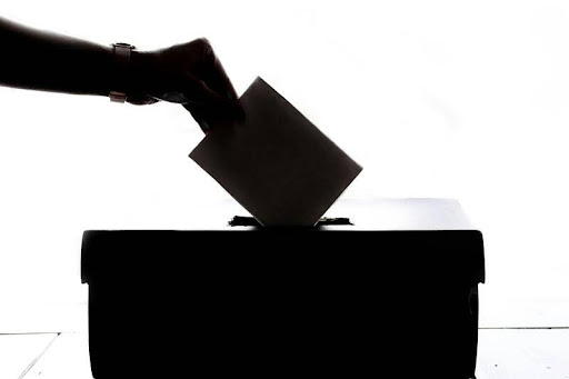 Person placing a voting ballot into a ballot box.