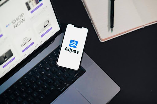 Smartphone showing AliPay app next to an open laptop on a desk