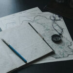 Book, pen, and map laid out on a wooden table.