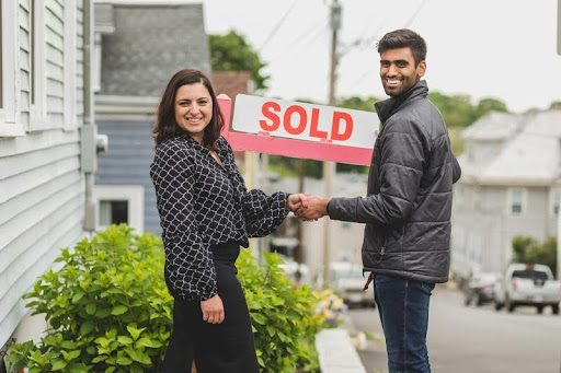 Woman and man shaking hands outside a modern building, symbolizing successful business partnership and real estate agreement.