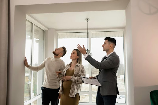 House seller guiding a couple through a modern home, highlighting spacious interiors and key features during a property tour.