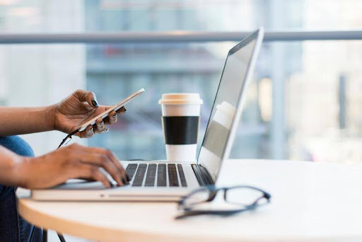 Person working on a laptop with a smartphone beside it on a clean table, capturing a modern digital workspace setup.