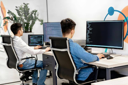 Two men working on laptops in a modern, minimalist room with black, white, and gold accents, focused on collaboration.