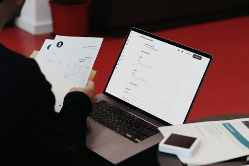 Person working at a modern desk with a laptop and papers, focused on productivity in a minimalist workspace.