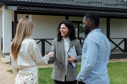 A smiling couple shakes hands with a real estate agent after closing a home deal in a modern, bright setting.