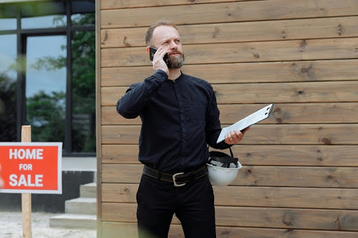 Man standing in front of a modern house with a “For Sale” sign, symbolizing a new real estate opportunity.