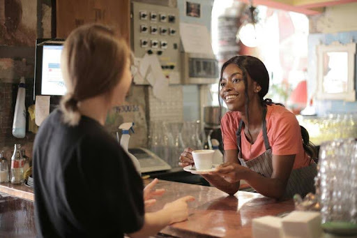 Woman in modern black and white uniform serving a customer, highlighting attentive service and professional interaction.