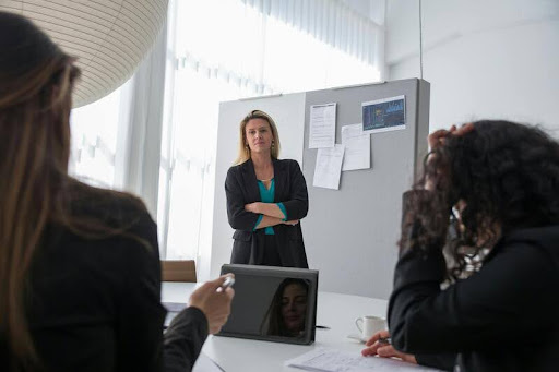 Woman presenting in a meeting, standing beside a screen as colleagues listen, conveying leadership and professional communication.