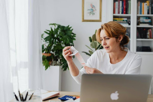 Woman reviewing a receipt while working on a laptop, highlighting budgeting and financial planning in a modern, minimalist workspace.