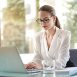 Female entrepreneur typing on a laptop at a sleek desk, focused on work in a modern, minimalist gold-and-black workspace.
