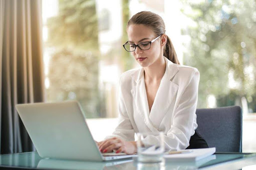 Female entrepreneur typing on a laptop at a sleek desk, focused on work in a modern, minimalist gold-and-black workspace.