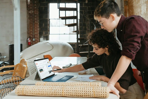 Woman showing a man something on her laptop as they review work together in a modern, minimalist workspace.